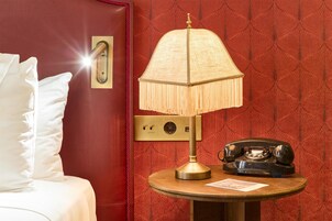 A hotel room with a bed, a lamp, a telephone, and a wall with a patterned design.