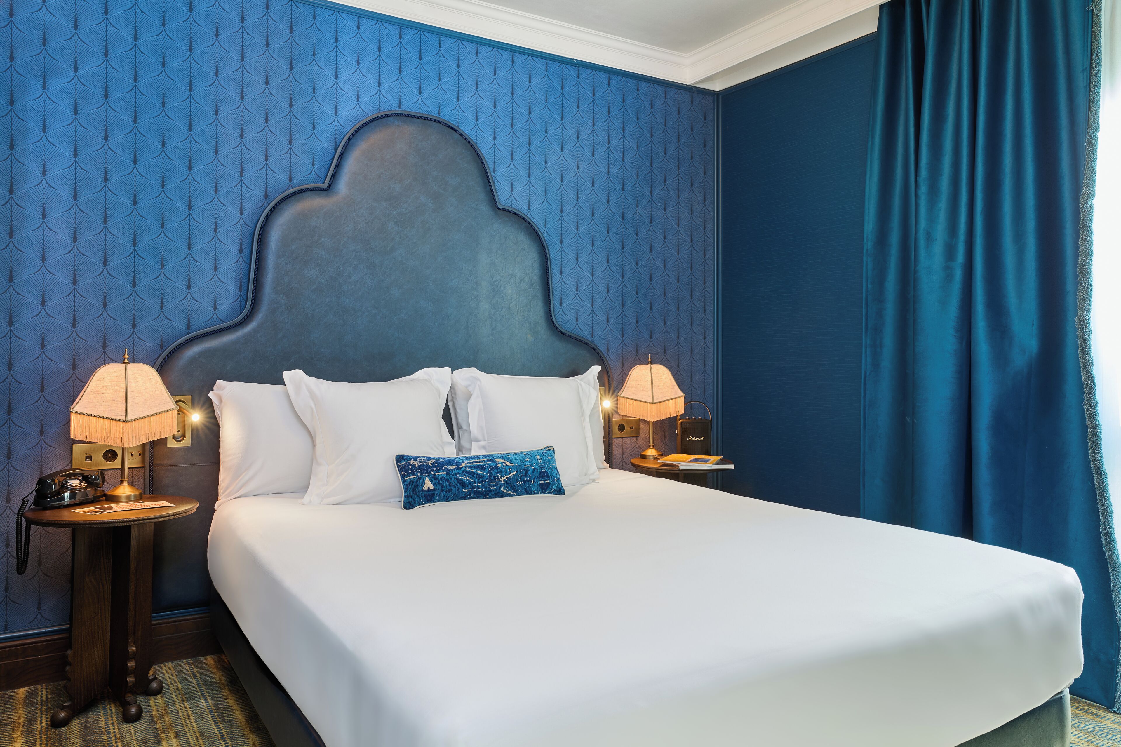 Habitación de hotel con una cama grande, dos lámparas de noche, un teléfono y un papel tapiz estampado.