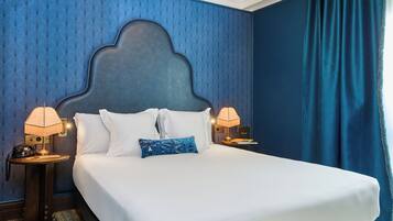 Habitación de hotel con una cama grande, dos lámparas de noche, un teléfono y un papel tapiz estampado.