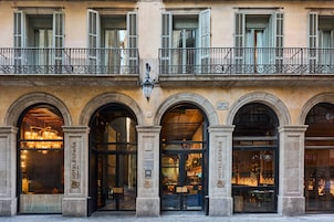 A hotel facade with multiple arched entrances, a balcony with wrought iron railings, and a street sign indicating the location.