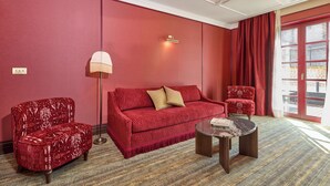 Habitación con decoración roja, un sofá, dos sillones, una lámpara de pie y una mesita de centro.