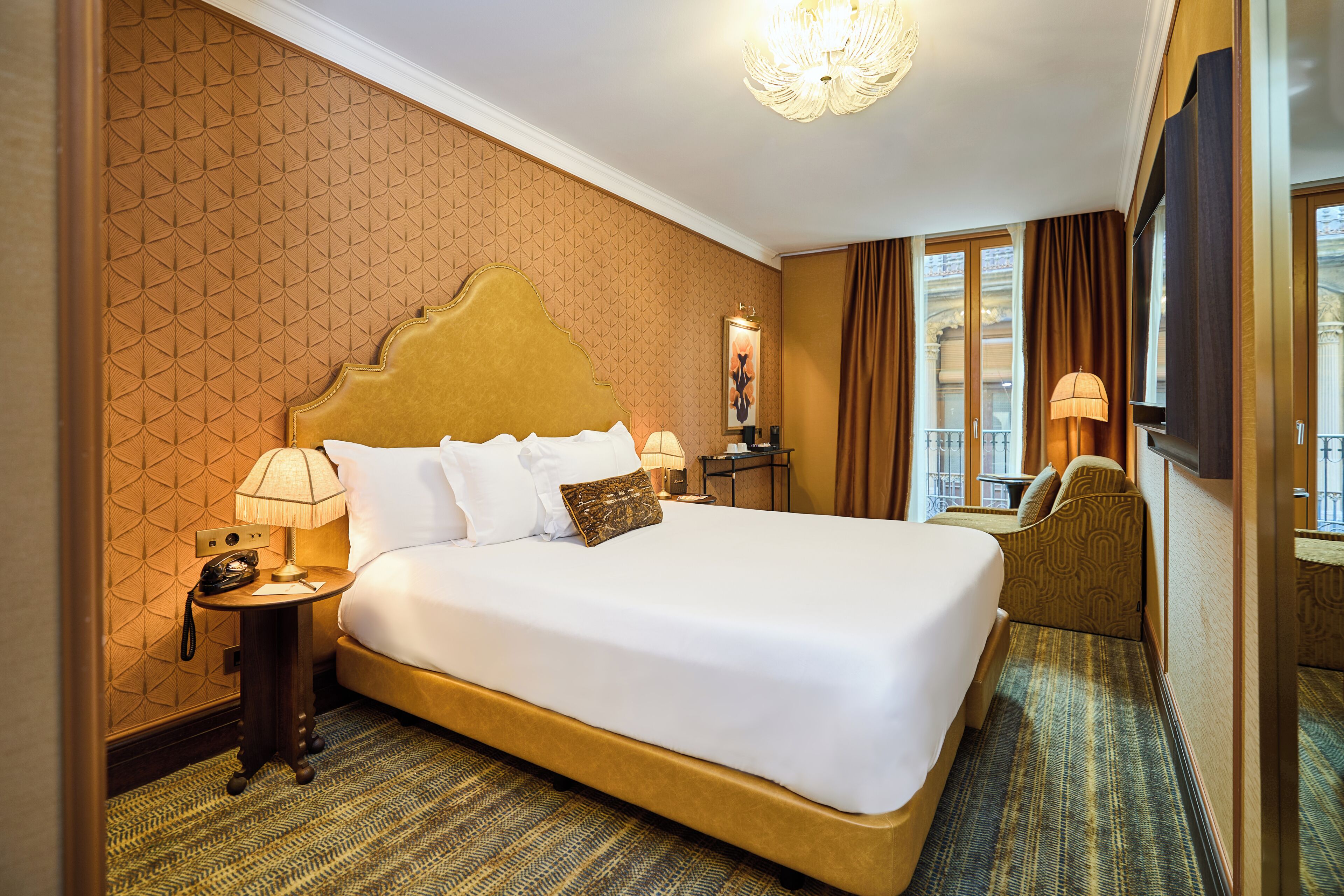 A hotel room with a large bed, a bedside table, a lamp, a chair, and a window with curtains.