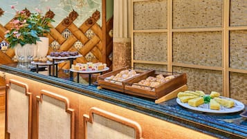 Un mostrador de buffet con diversos alimentos, entre ellos pasteles y postres, y una pared decorativa con un diseño geométrico.