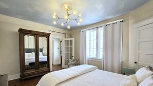A bedroom with a large bed, a mirror, a chandelier, and a window with curtains. - UPTOWN OASIS W PRIVATE, HEATED POOL, Minutes to all New Orleans' top attractions (New Orleans)