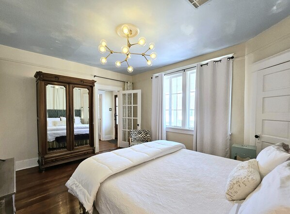 Un dormitorio con una cama grande, un espejo, una araña de cristal y una ventana con cortinas.
