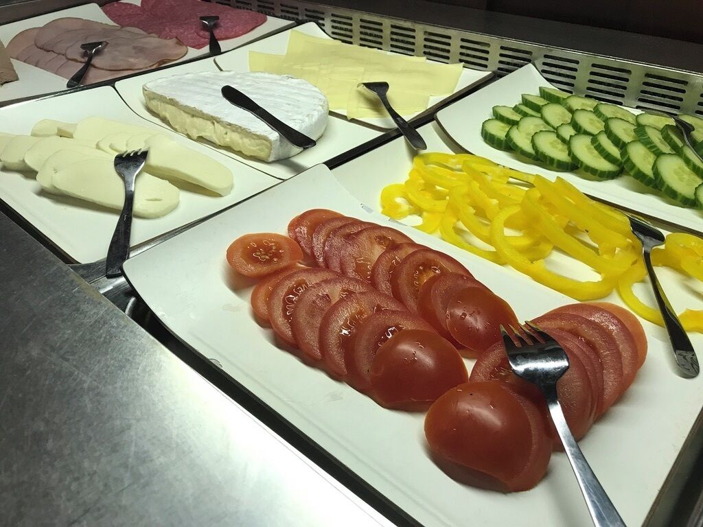Un bufé con diversos alimentos, como tomates en rodajas, pimientos amarillos, pepinos, queso y jamón.