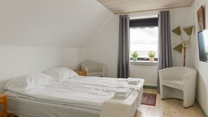 A bedroom with a bed, two chairs, a window with curtains, a radiator, and a lamp. - Branteviks Bed & Breakfast (Brantevik)