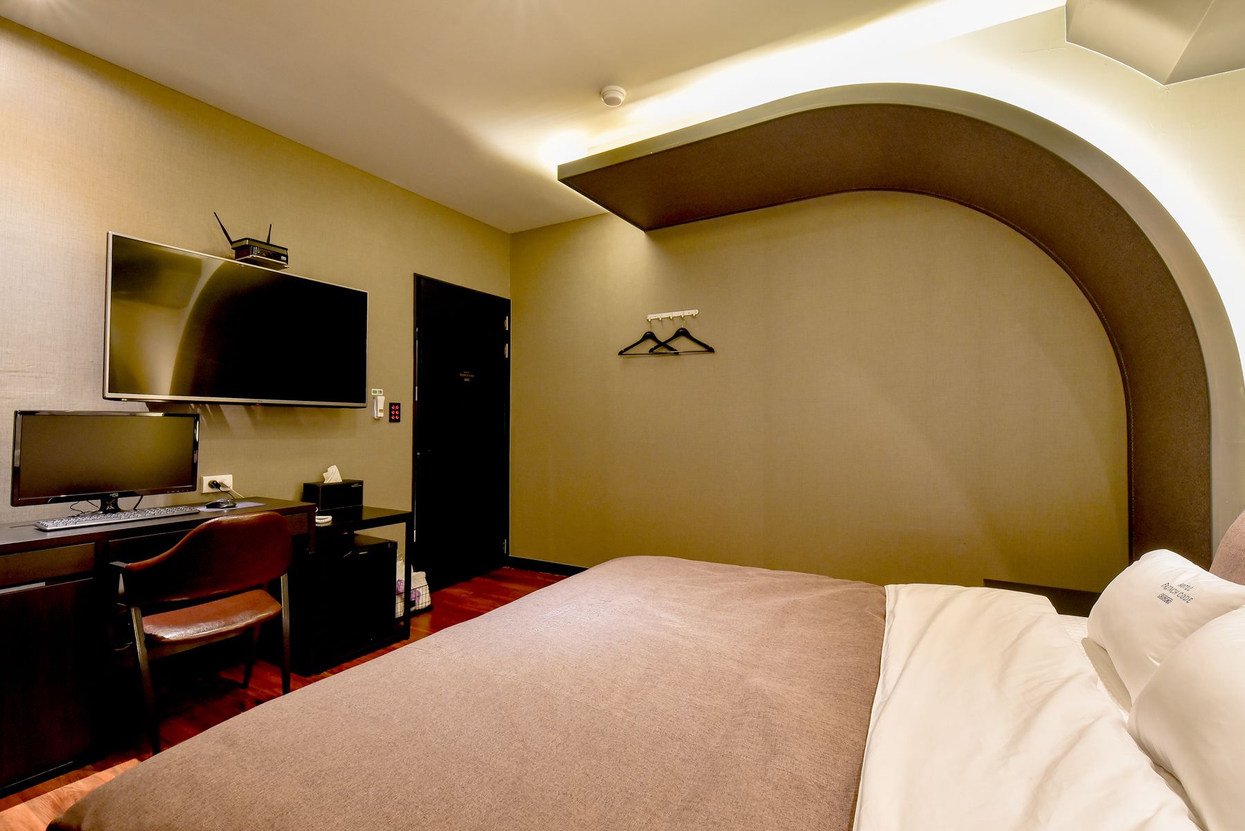 A hotel room with a bed, desk, chair, television, and a coat rack.