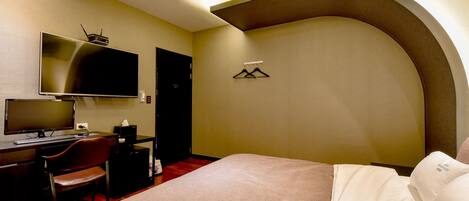 A hotel room with a bed, desk, chair, television, and a coat rack.