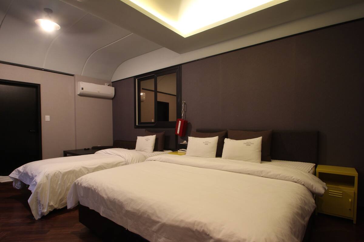A hotel room with two beds, a bedside table, a nightstand, a mirror, and an air conditioning unit.