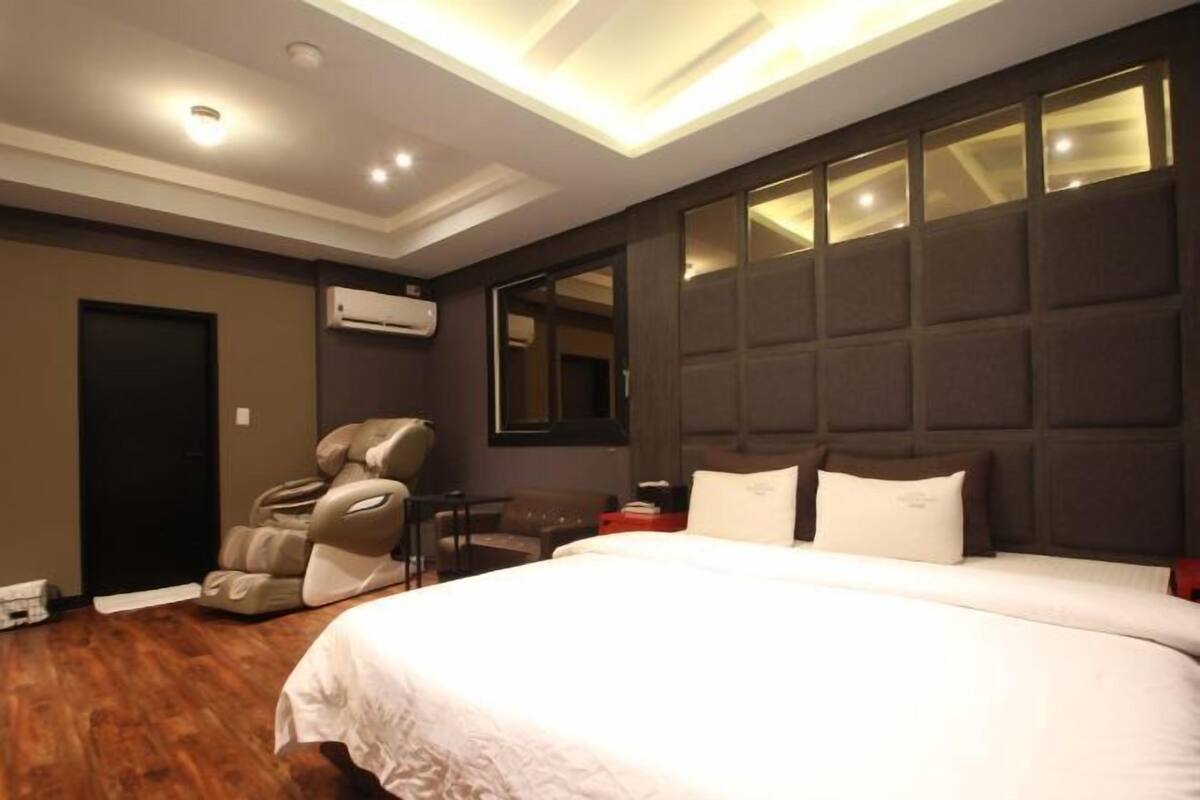 A hotel room with a large bed, massage chair, and a wall-mounted air conditioner.