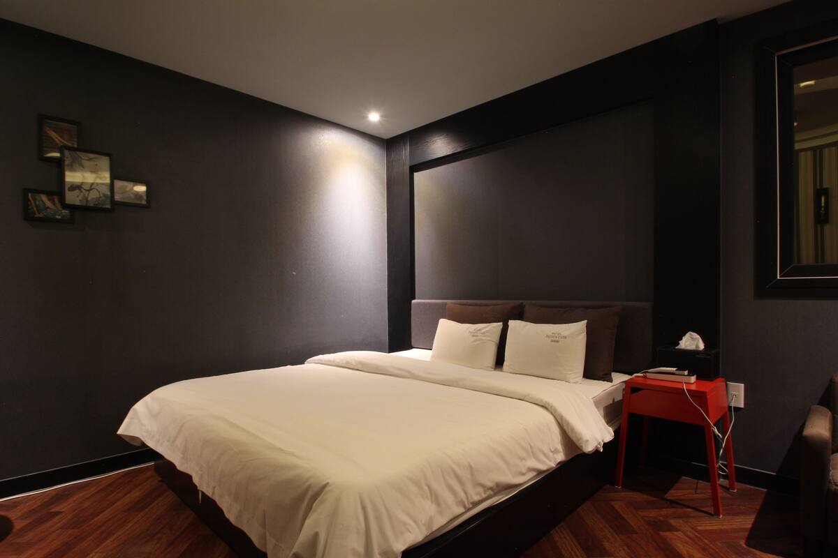 A modern bedroom with a large bed, dark walls, and a small bedside table.