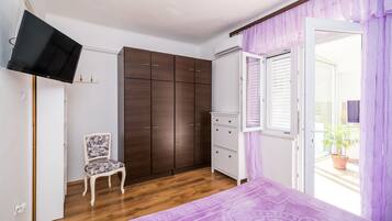 Une chambre à coucher comprenant un lit, une armoire, une chaise, un téléviseur et une fenêtre avec des stores.