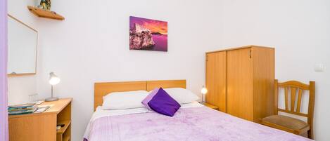 A bedroom with a bed, a wooden wardrobe, a desk with a lamp, and a wall-mounted picture.
