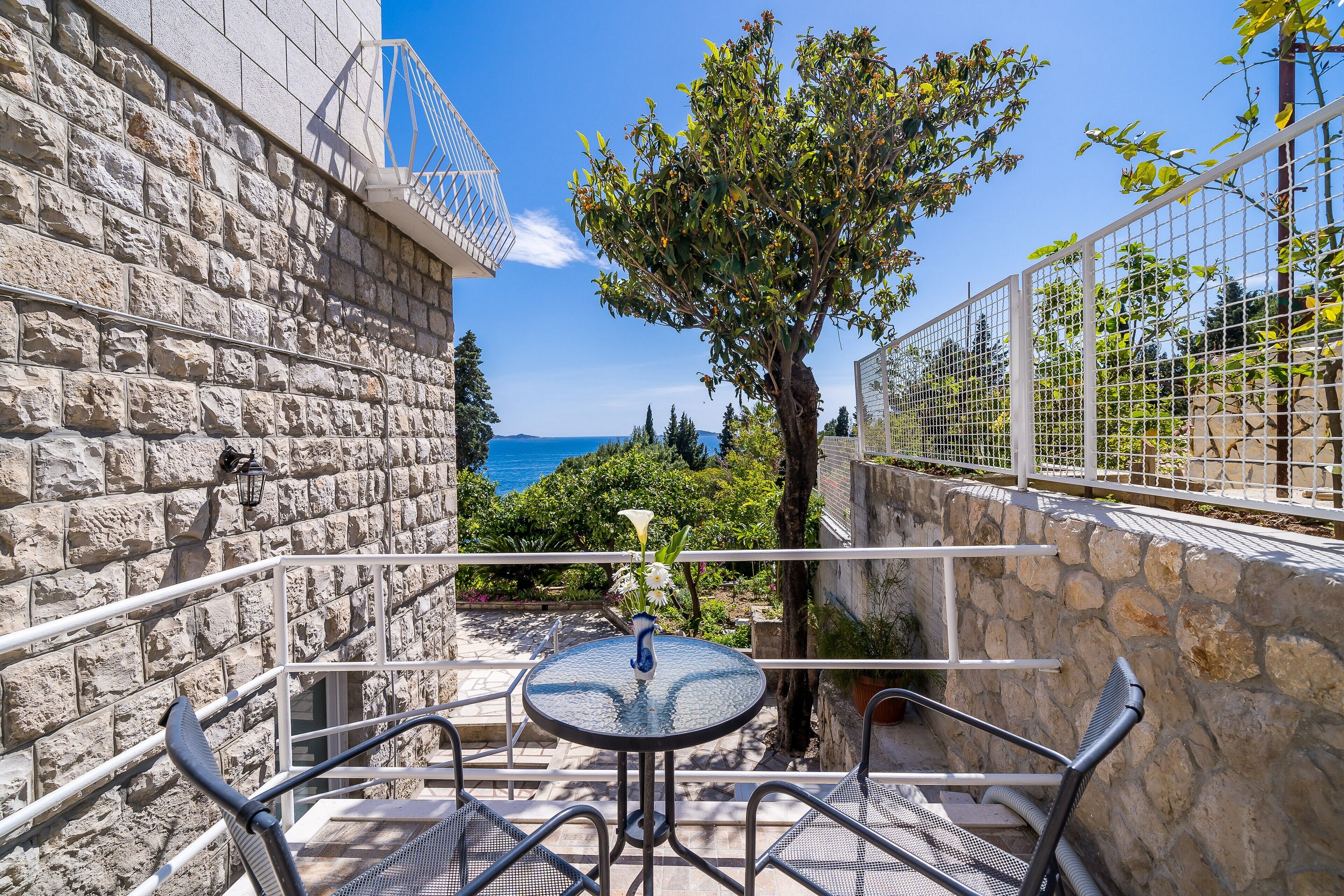 A stone building with a balcony, outdoor seating, and a view of the sea.