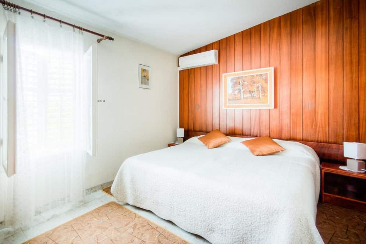 Een slaapkamer met een groot bed, houten paneelwanden, een raam met gordijnen en een ingelijst schilderij aan de muur.