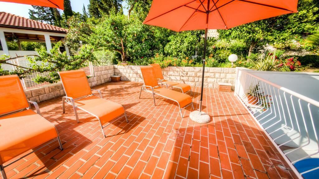 Un patio al aire libre con sillas naranjas y un paraguas rojo.