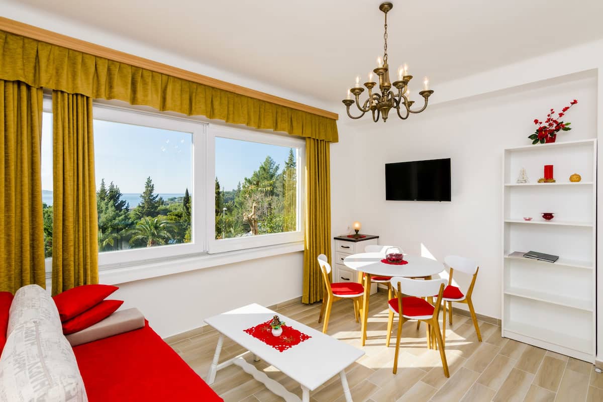 Een moderne woonkamer met een bank, eettafel, stoelen, een televisie en een raam met gordijnen.