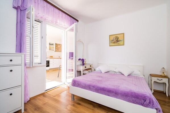 Un dormitorio con cama, mesita de noche, cómoda y puerta que da a una cocina.