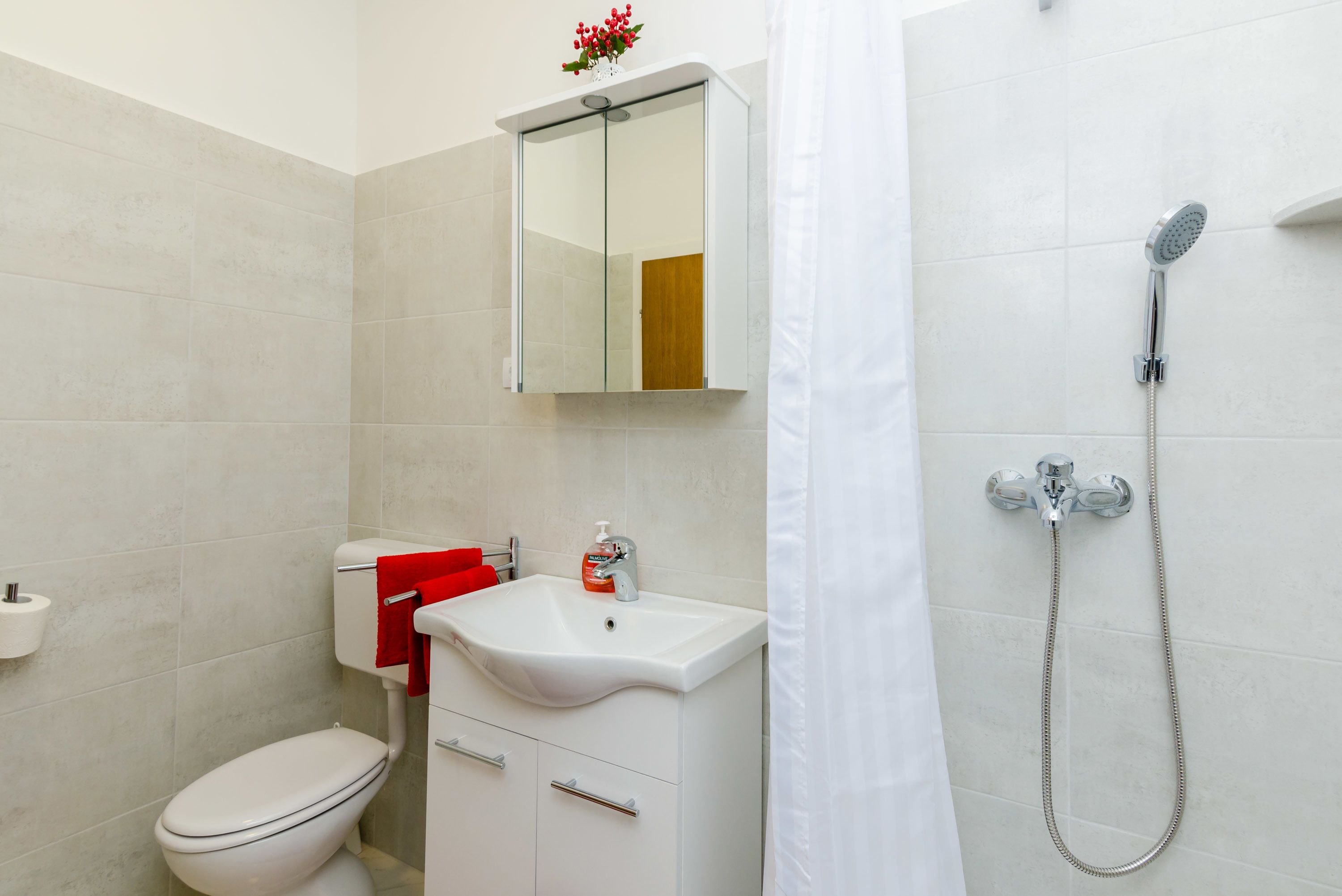 A bathroom with a toilet, sink, mirror, and shower.