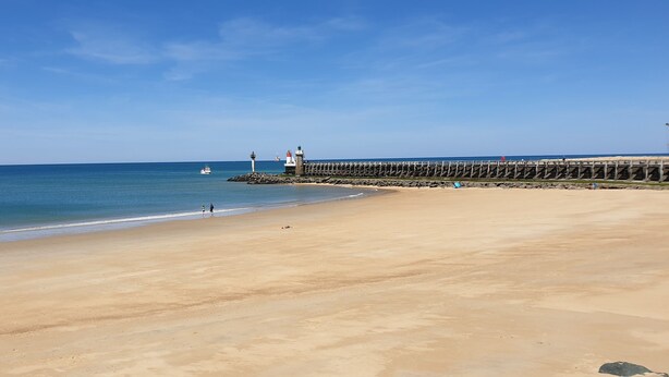 A wide sandy beach with a rocky breakwater and a lighthouse in the background. - Hôtel La Baïne (Capbreton)