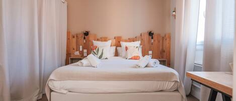 Una cama bien hecha con almohadas y toallas, cabecera de madera y mesita de noche con lámpara.