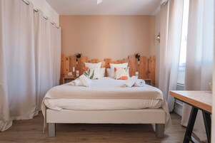 Una cama bien hecha con almohadas y toallas, cabecera de madera y mesita de noche con lámpara.