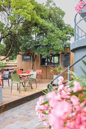 Un área exterior con mesas y sillas, una valla de madera y un letrero para una pizzería.