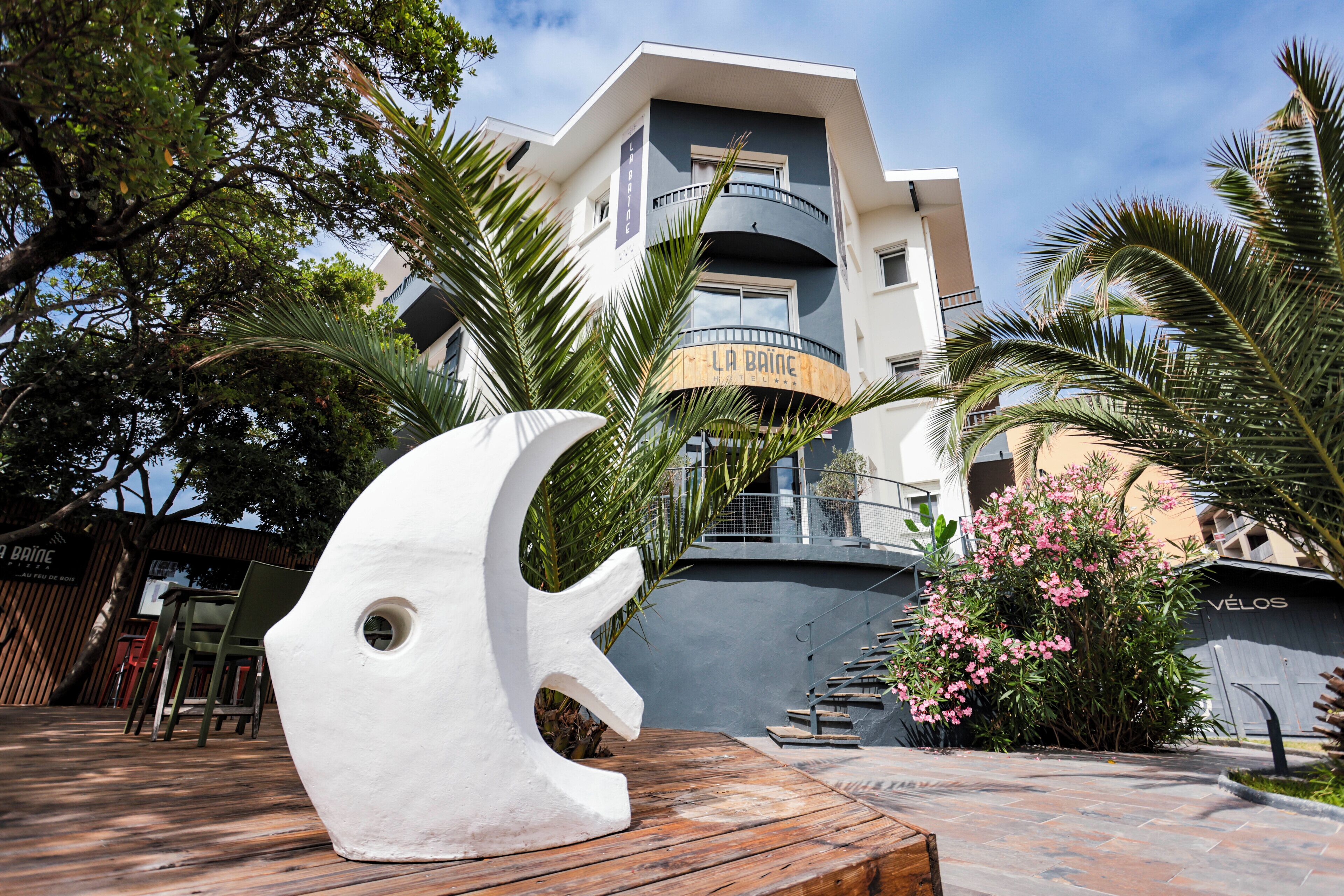 A modern building with a sign reading 'LA BAINE HOTEL' and a large white sculpture in the foreground.
