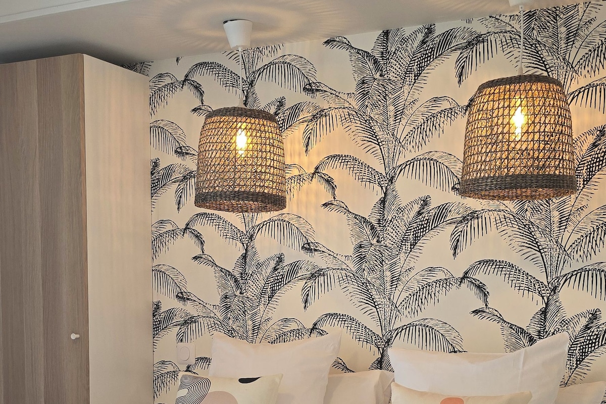 A neatly made bed with a rolled towel, a patterned wall, and two hanging lamps.