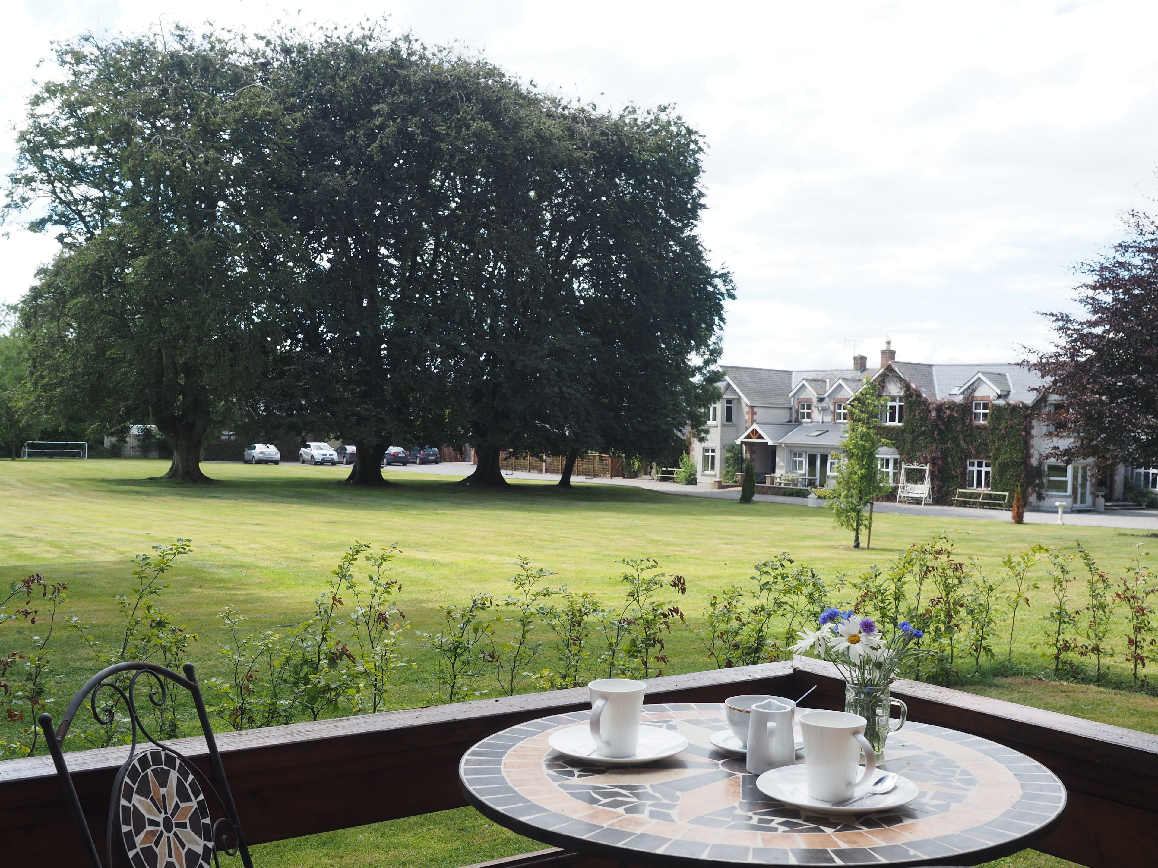 A patio with a table set for two, overlooking a well-maintained lawn and a large tree.