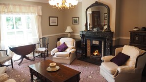 Un salón tradicional con chimenea, dos sillones, una mesa de centro de madera y una araña.