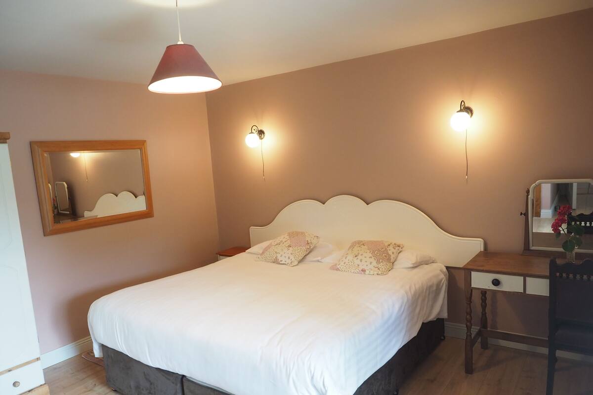 A neatly made bed with a white headboard, a bedside table with a mirror, and two wall-mounted lights.