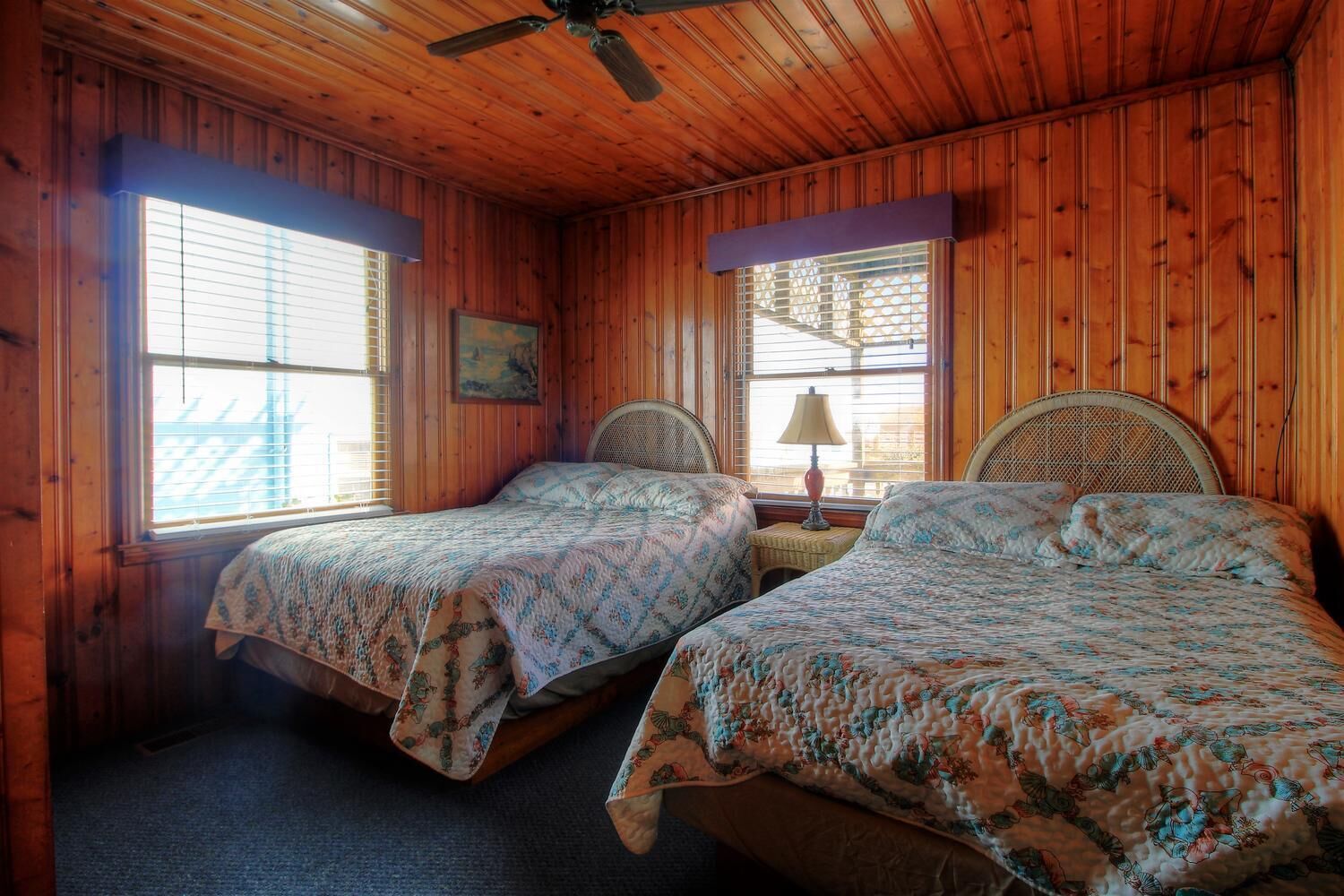 A cabin with two beds, wooden walls, and a ceiling fan.