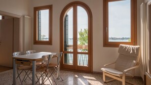Una habitación con una mesa de comedor, sillas, un sillón acolchado y ventanas amplias con vista al mar.