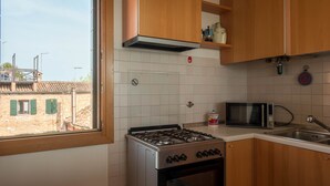 Una cocina con gabinetes de madera, estufa a gas, microondas y ventana con vista a edificios.