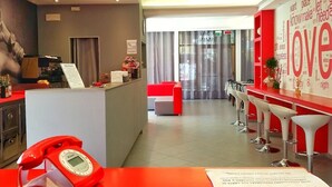 Eine moderne Hotellobby mit einer Rezeption, einem roten Telefon und einer Bar mit weißen Barhocker.