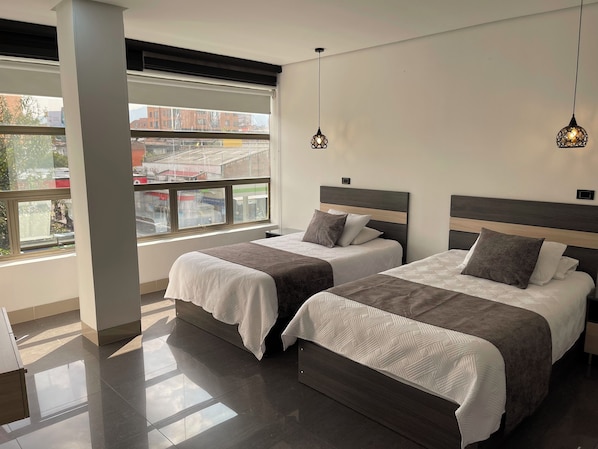 A hotel room with two beds, a large window, and pendant lighting. - Hotel Merlott 70 (Medellín)