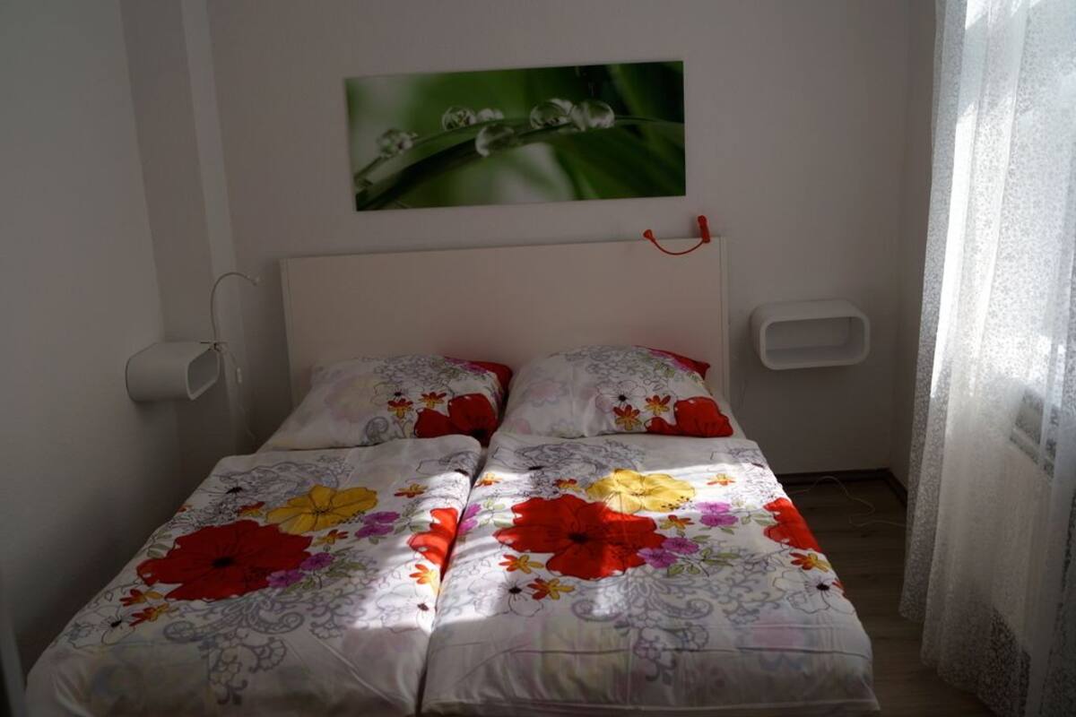 Una cama con ropa de cama floral, cabecera blanca y un cuadro colgado en la pared.