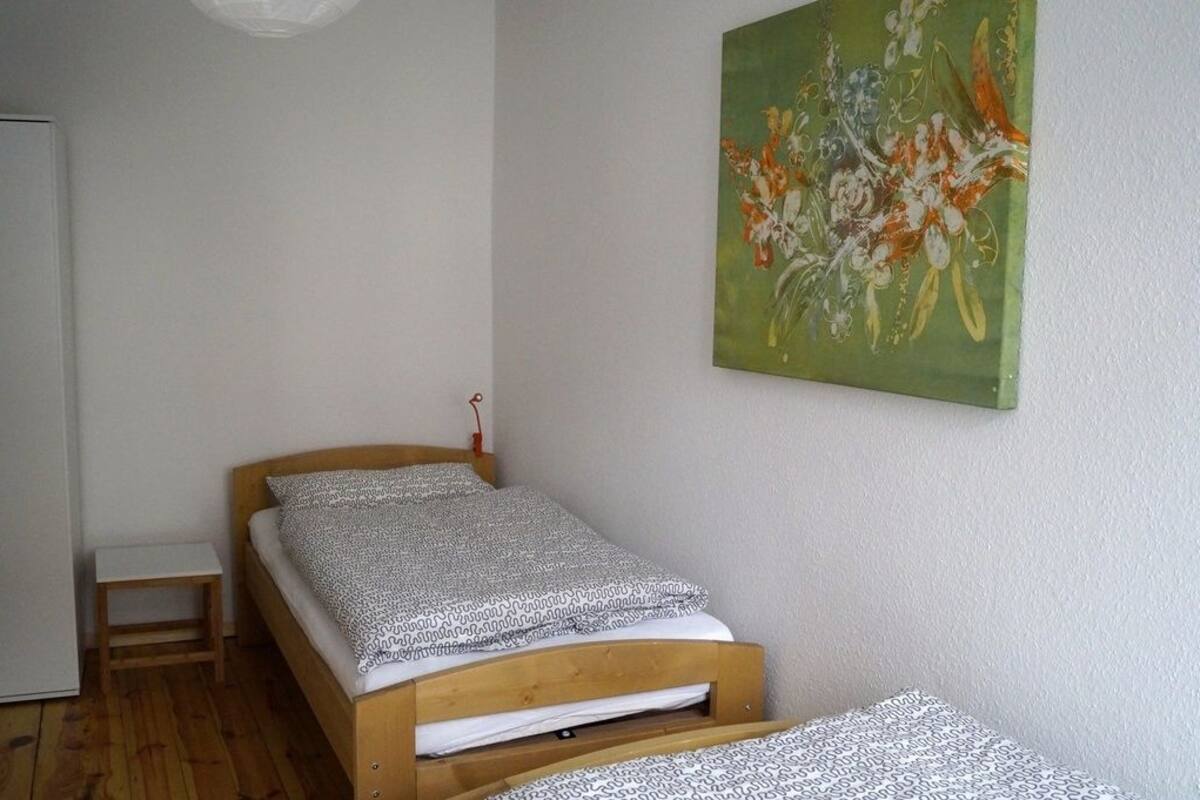 Un dormitorio pequeño con una cama individual, una mesita de noche de madera y un cuadro abstracto verde en la pared.