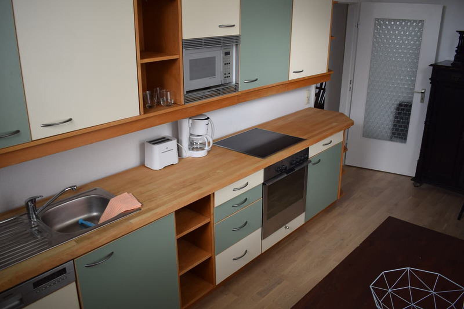 A compact kitchen with a microwave, toaster, and coffee maker on the countertop, wooden cabinets, and a dishwasher.
