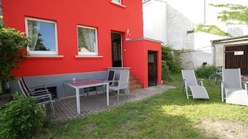 Un edificio rojo con un patio que incluye una mesa, sillas, una bicicleta y un jardín.