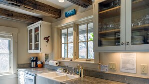 Una cocina con armarios blancos, un lavamanos grande y una ventana con vistas a árboles.