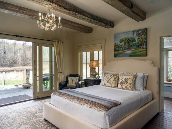 A bedroom with a large bed, a chandelier, a painting, and a view of a lake through a glass door.