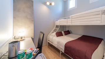 A bunk bed room with a desk, chair, and a small table with a lamp and a can.