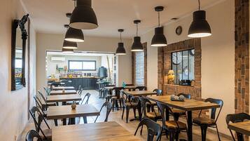 A spacious dining area with multiple wooden tables and black chairs, large pendant lights, and a brick accent wall.