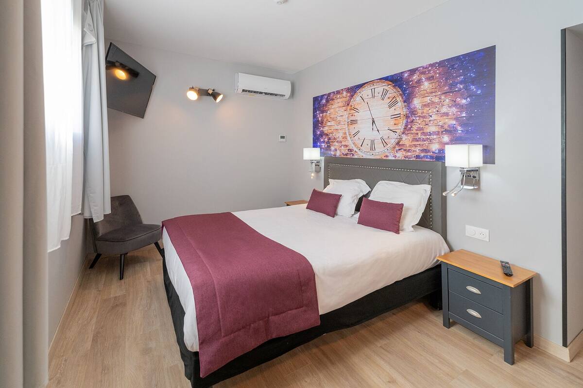 Une chambre d’hôtel moderne équipée d’un grand lit, d’un bureau, d’une chaise et d’un téléviseur fixé au mur.