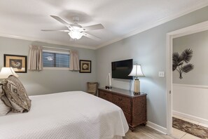 Un dormitorio con cama, cómoda, ventilador de techo, televisor y planta en la pared.