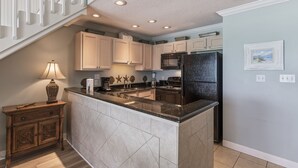 A kitchen with a central island, white cabinets, a black refrigerator, and a staircase leading to an upper level. - 38- Quaint, family friendly, 3 story condo on the gorgeous EMERALD COAST! (Destin)