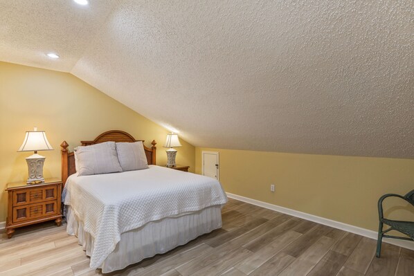 A bedroom with a bed, two bedside tables with lamps, a chair, and a door.